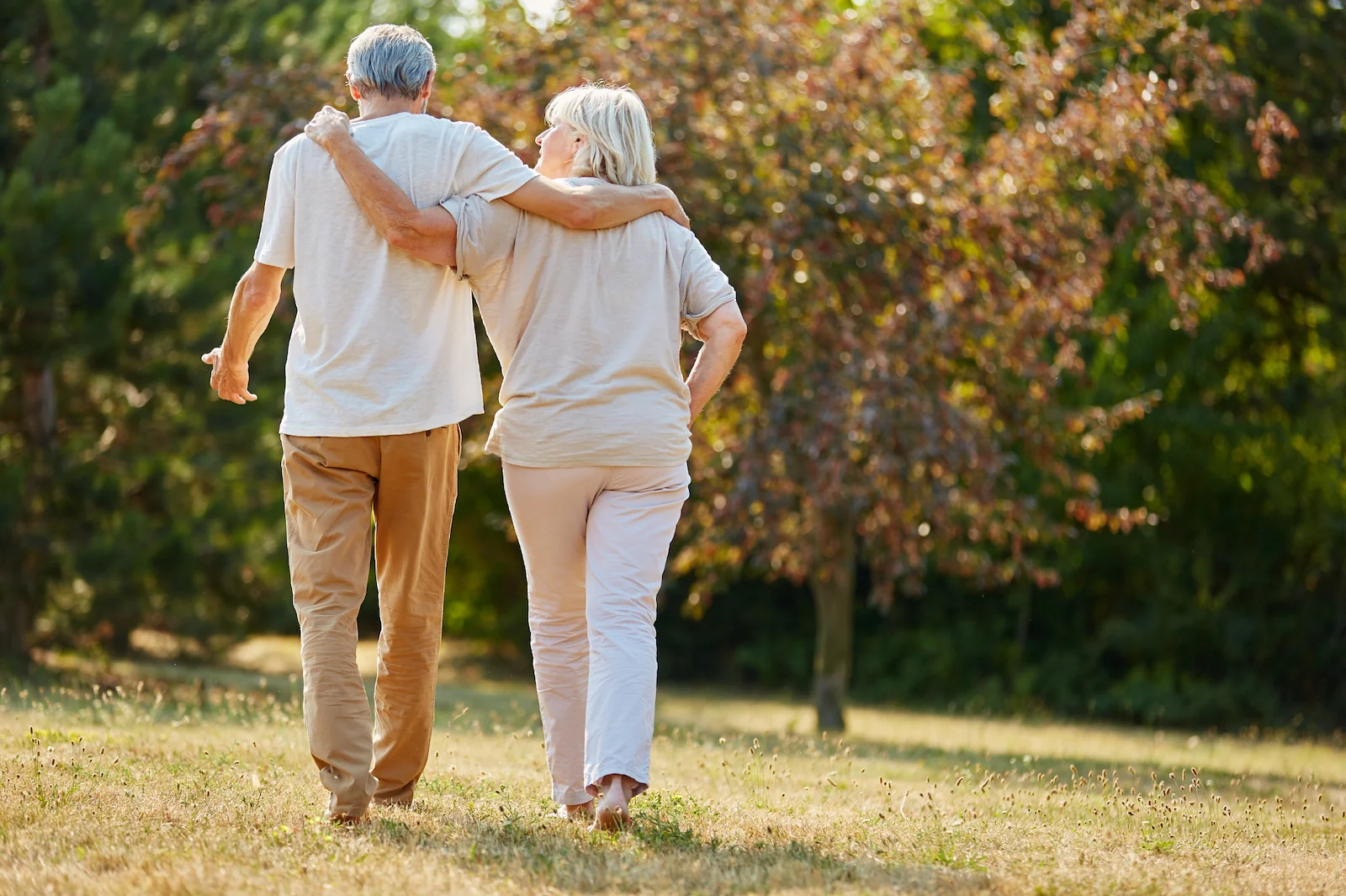 Senior couple walking arm in arm through a sunny park in autumn
