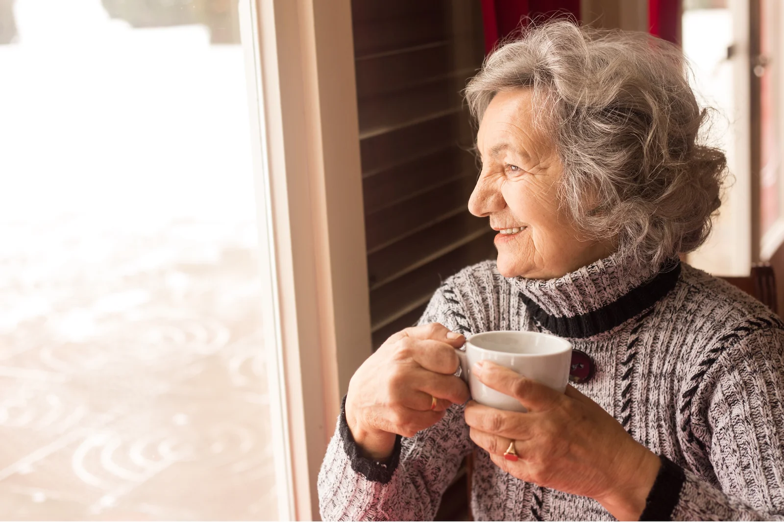 Smiling senior woman enjoying morning coffee while looking out a sunny window
