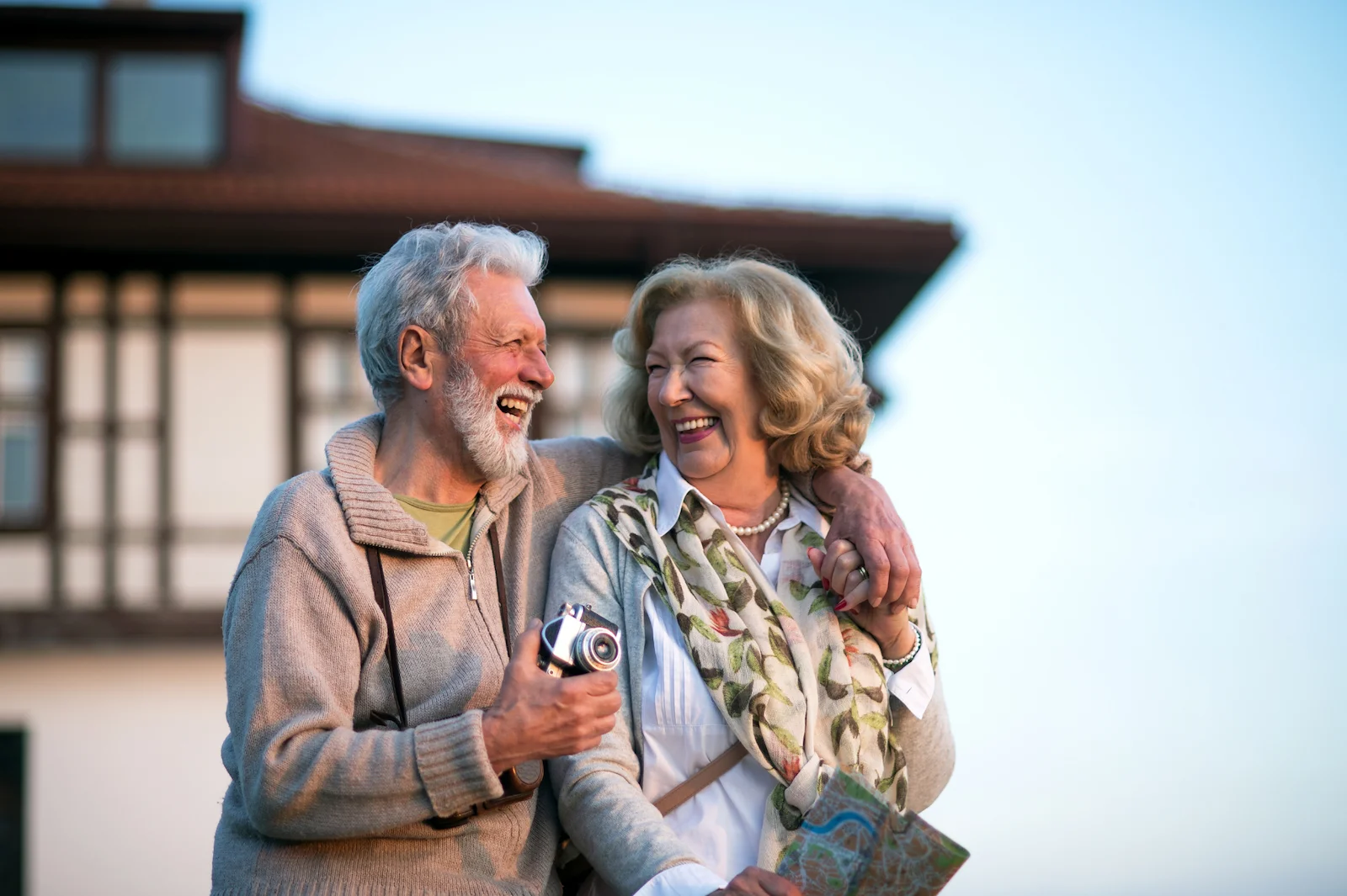 Cheerful senior couple laughing together while sightseeing with a camera on vacation