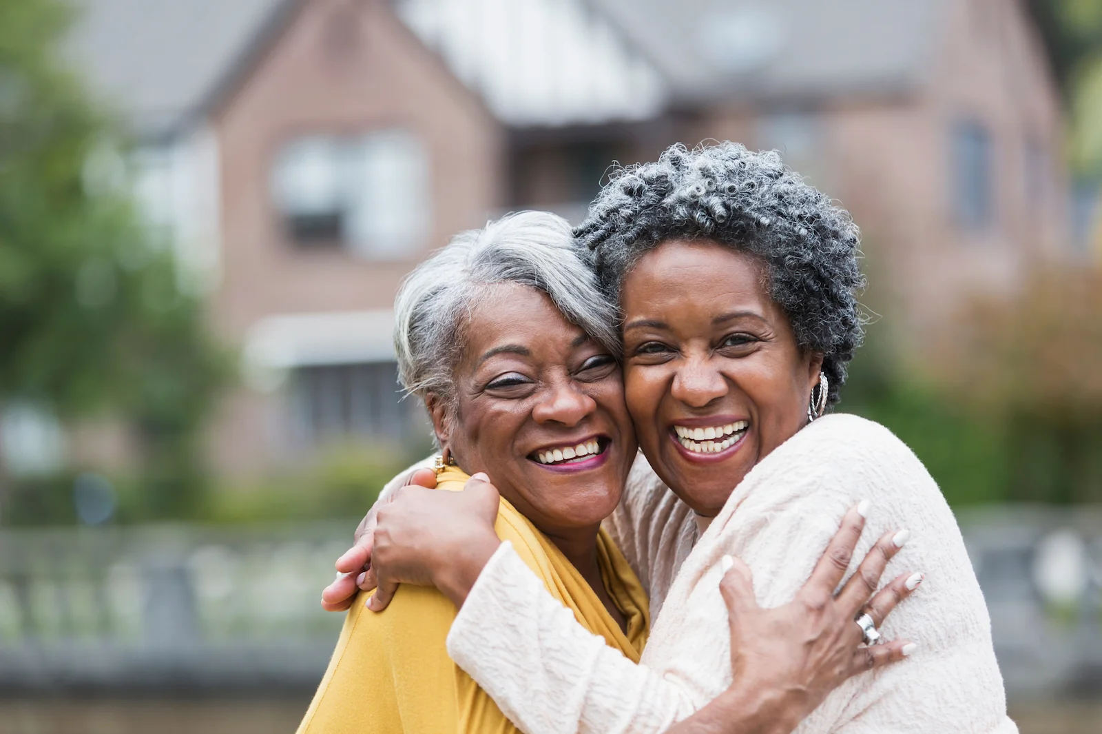 Two smiling senior women embracing in front of modern homes in active adult communities near you