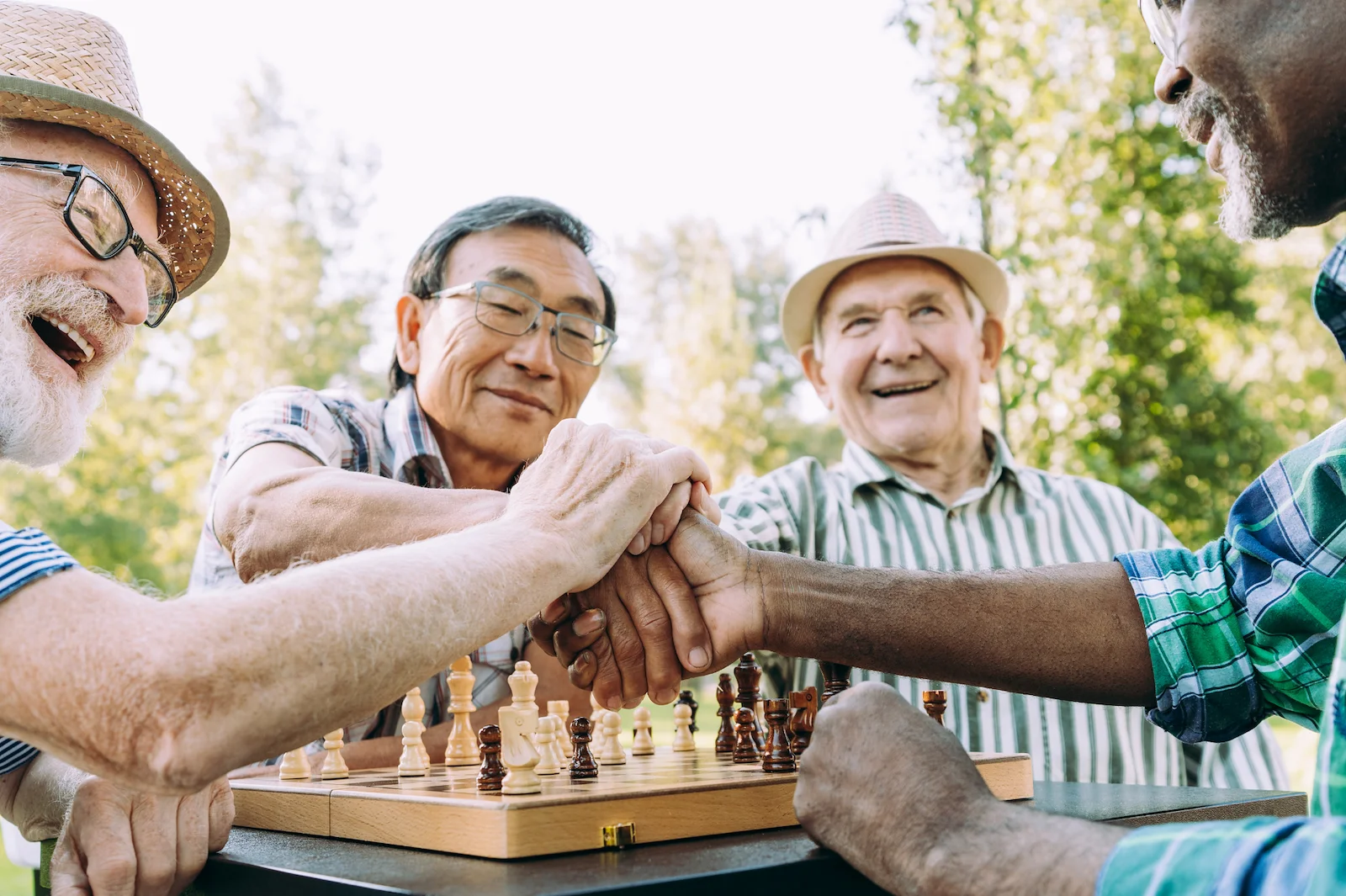 Group of senior men stacking hands together over a chess game outdoors