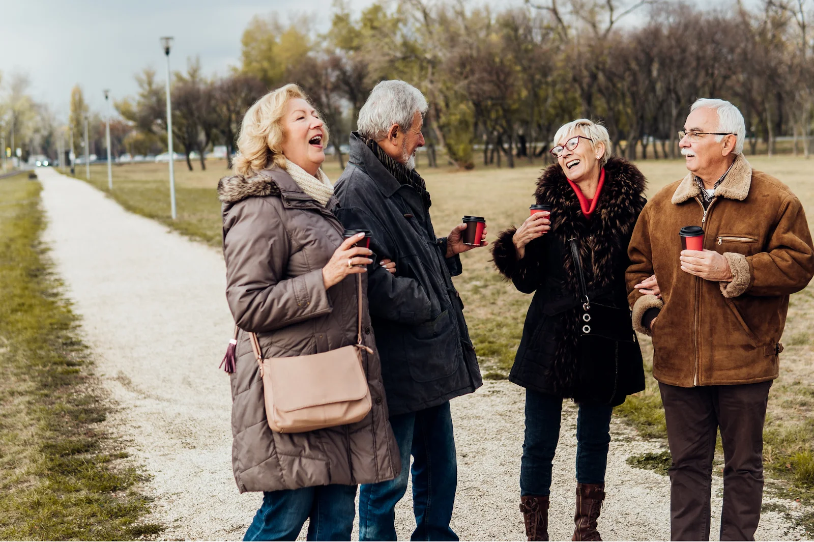 Group of senior friends laughing and enjoying coffee during a walk in the park