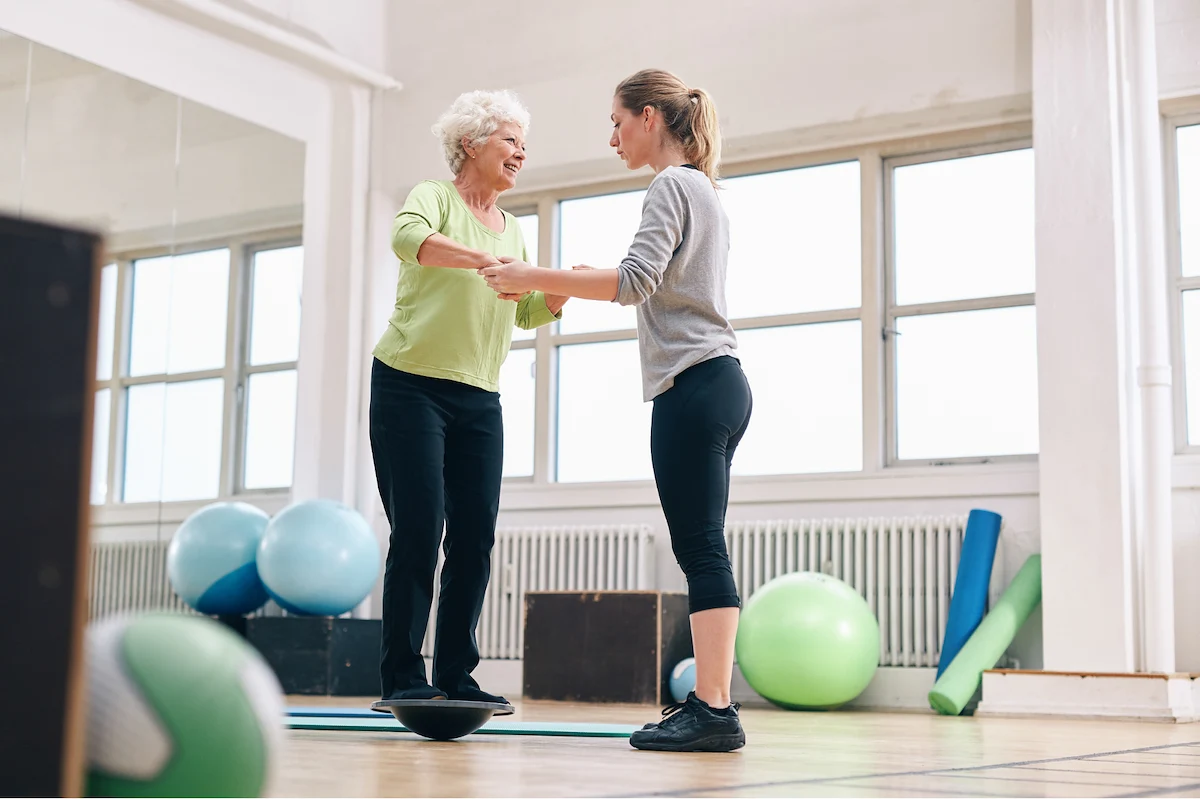 Physical therapist helping senior woman with balance exercises on a stability board
