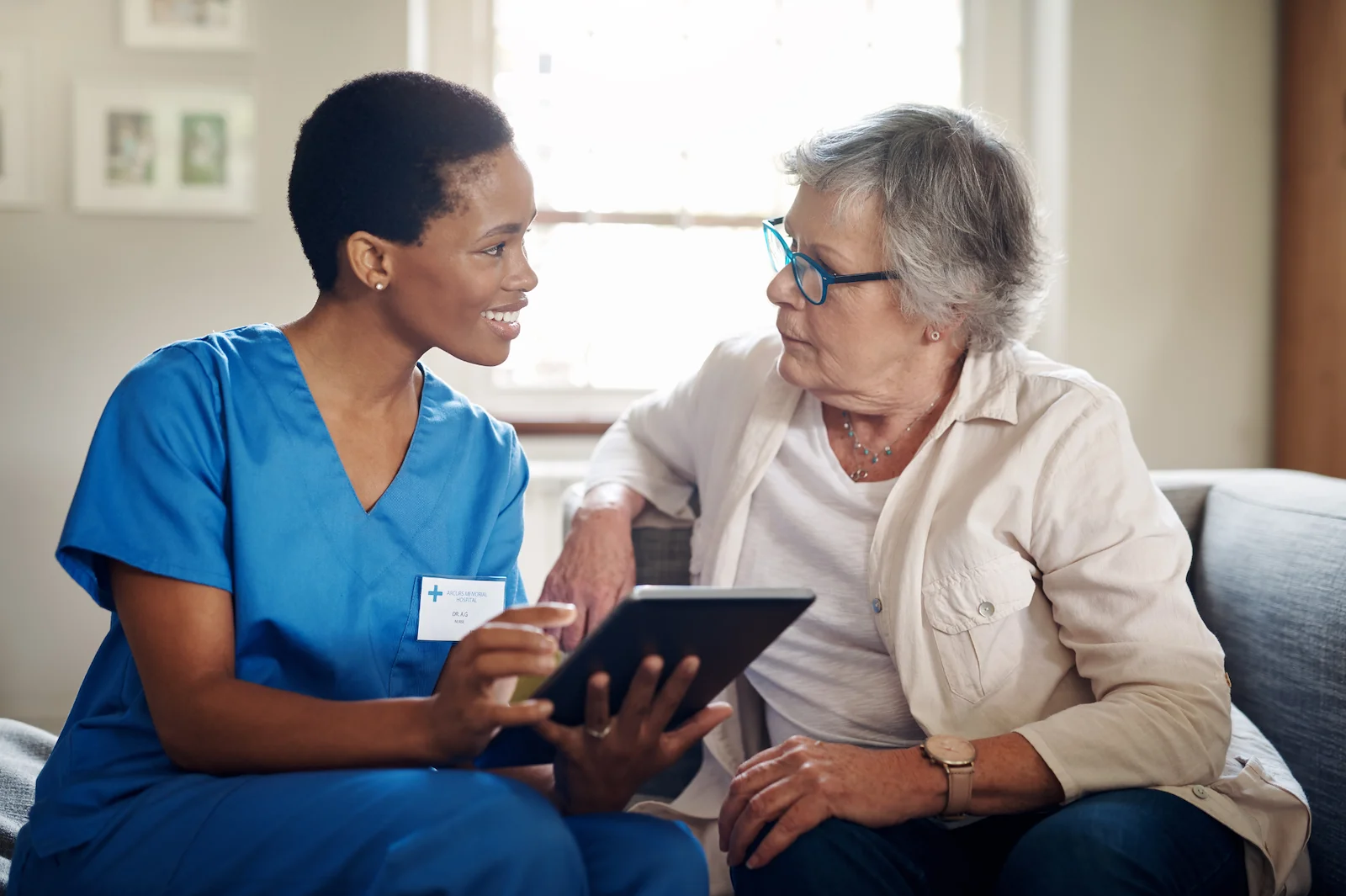 Healthcare professional consulting with senior woman using a tablet at home