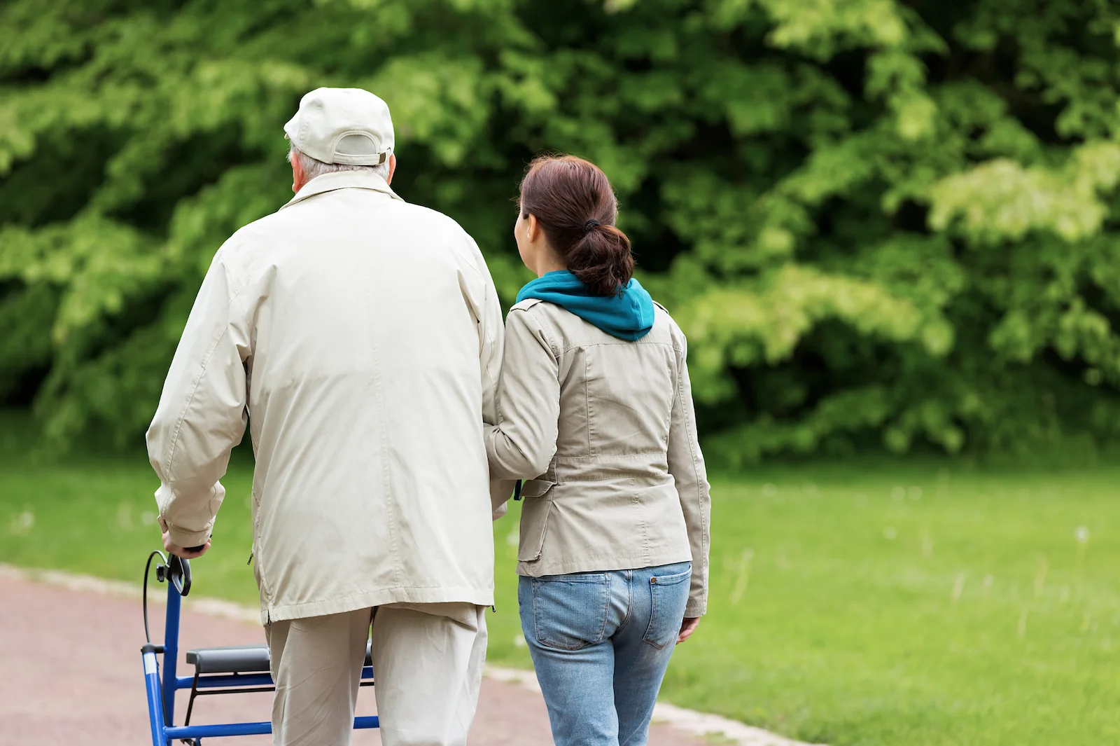 Caregiver walking alongside senior man with rollator walker on a park path