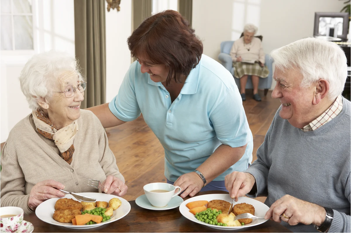 Caregiver serving meals to senior residents in a community dining area