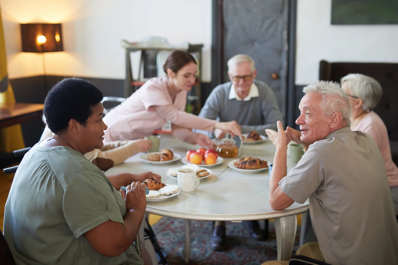 Caregiver pouring coffee for seniors enjoying breakfast together at a dining table