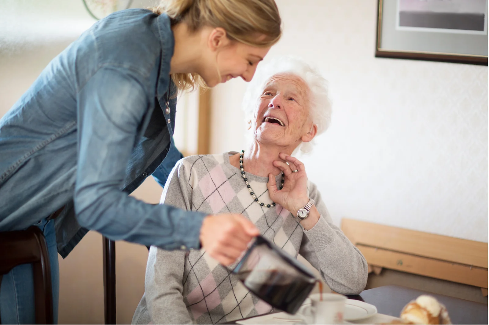 Caregiver helping senior woman put on a cardigan in a private bedroom