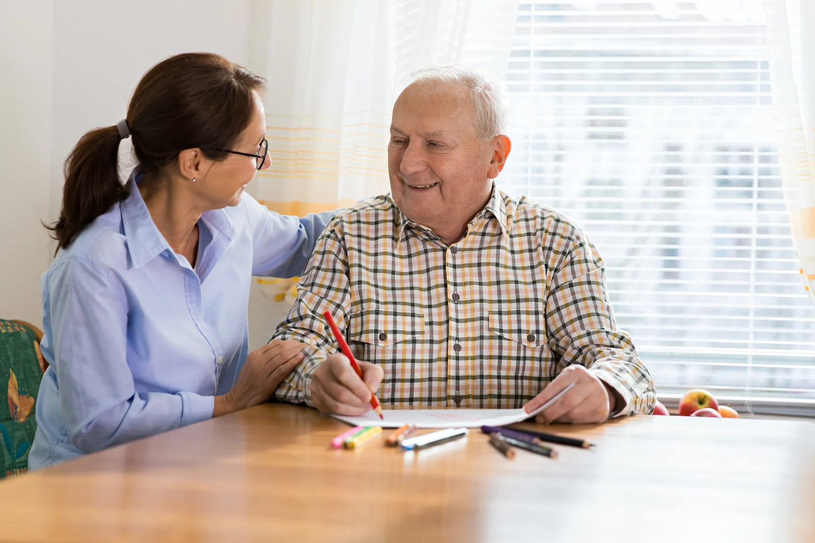 Caregiver supporting senior man during art therapy activity at home