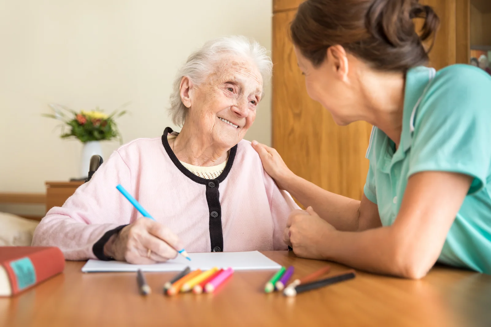 Caregiver assisting senior woman with drawing and art activities at home
