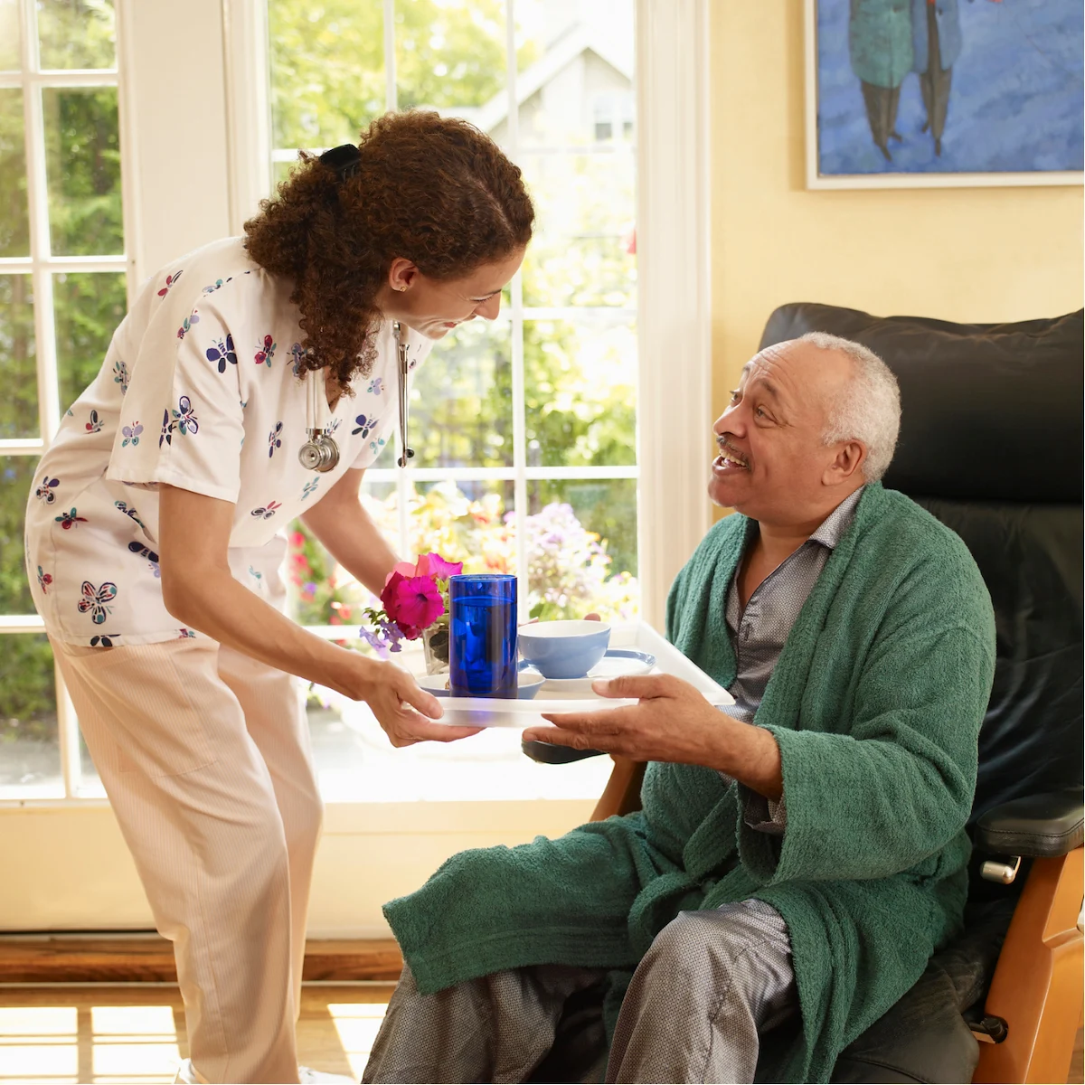 Home health aide bringing meal tray to senior man in a recliner