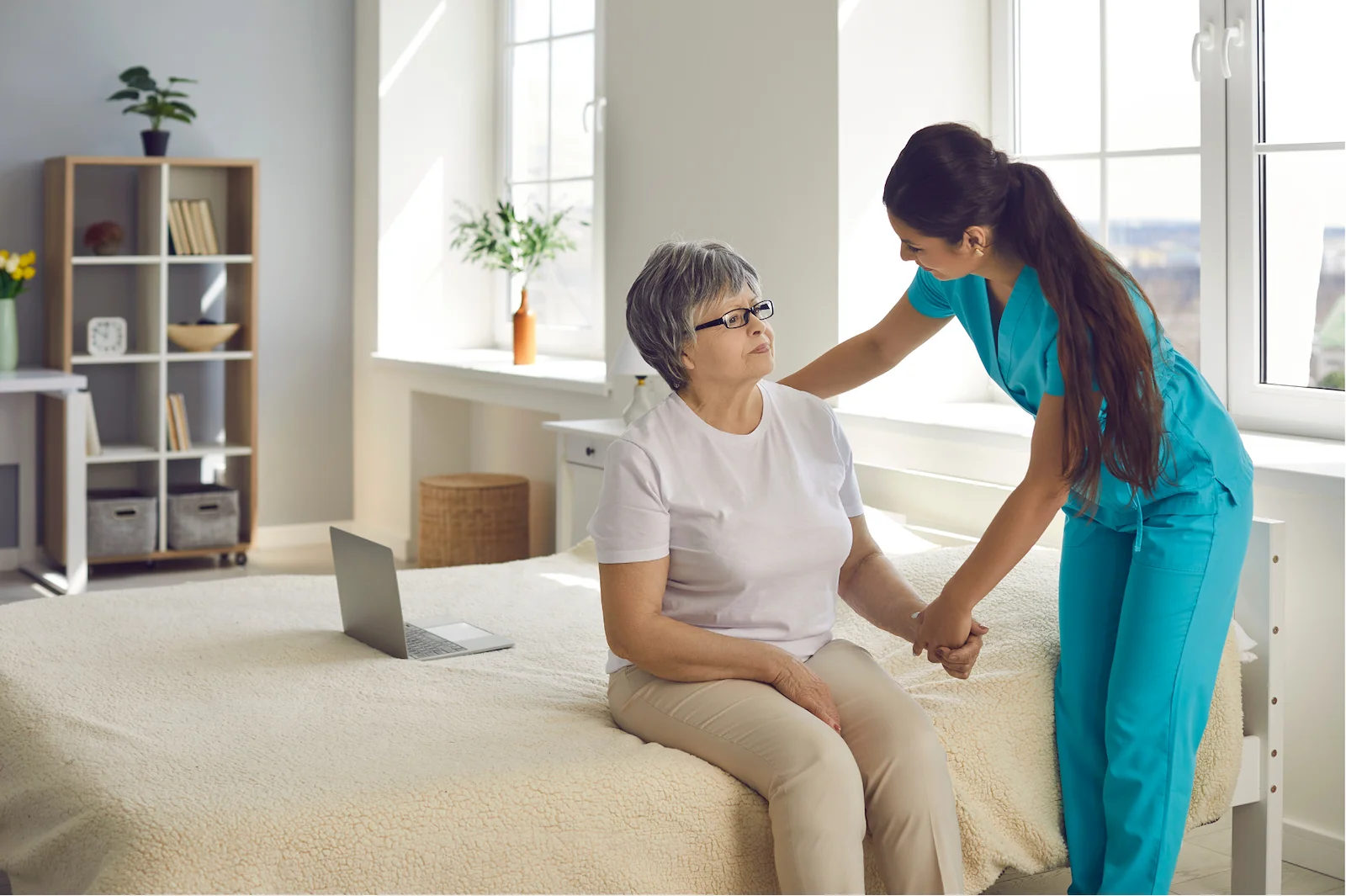 Nurse helping senior woman stand from bed in a sunny bedroom