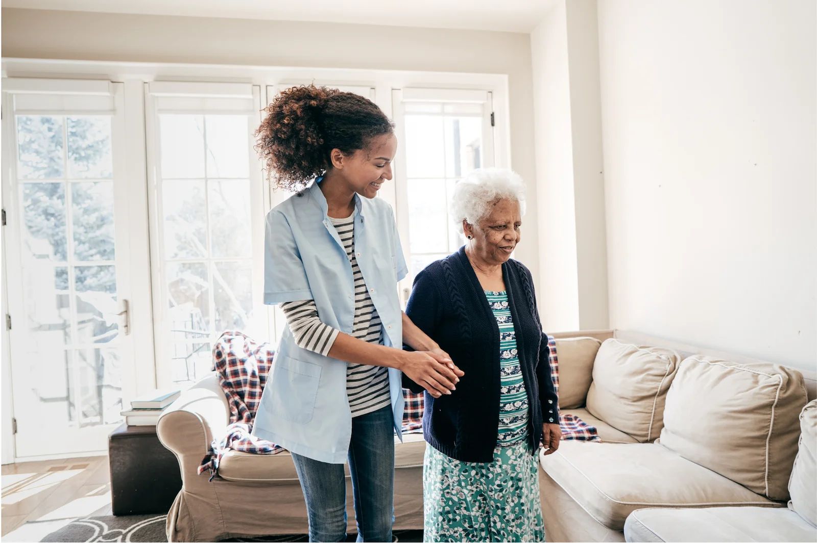 Caregiver assisting senior woman with mobility in a bright living room