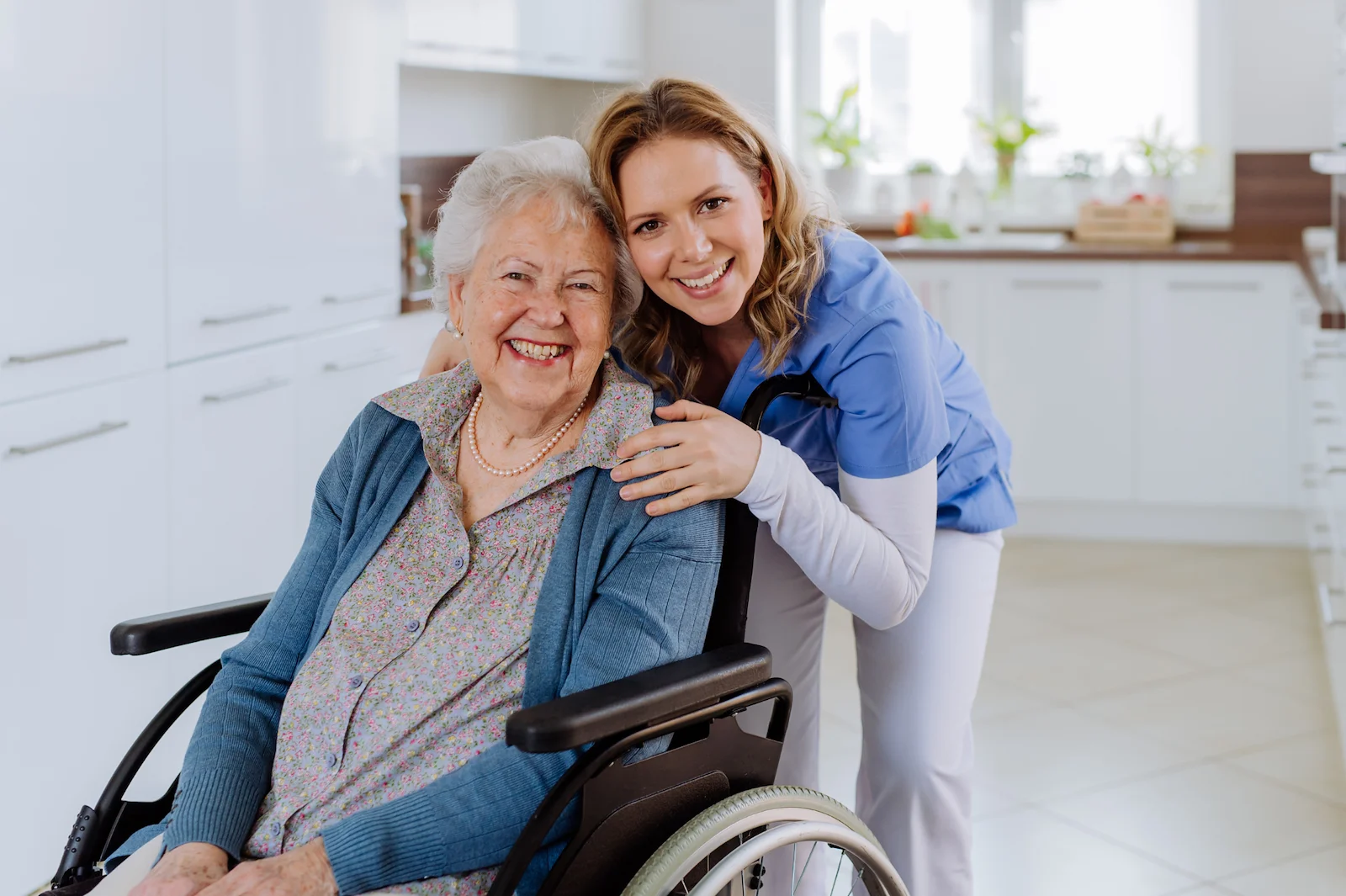 Smiling caregiver with senior woman in wheelchair in a modern kitchen