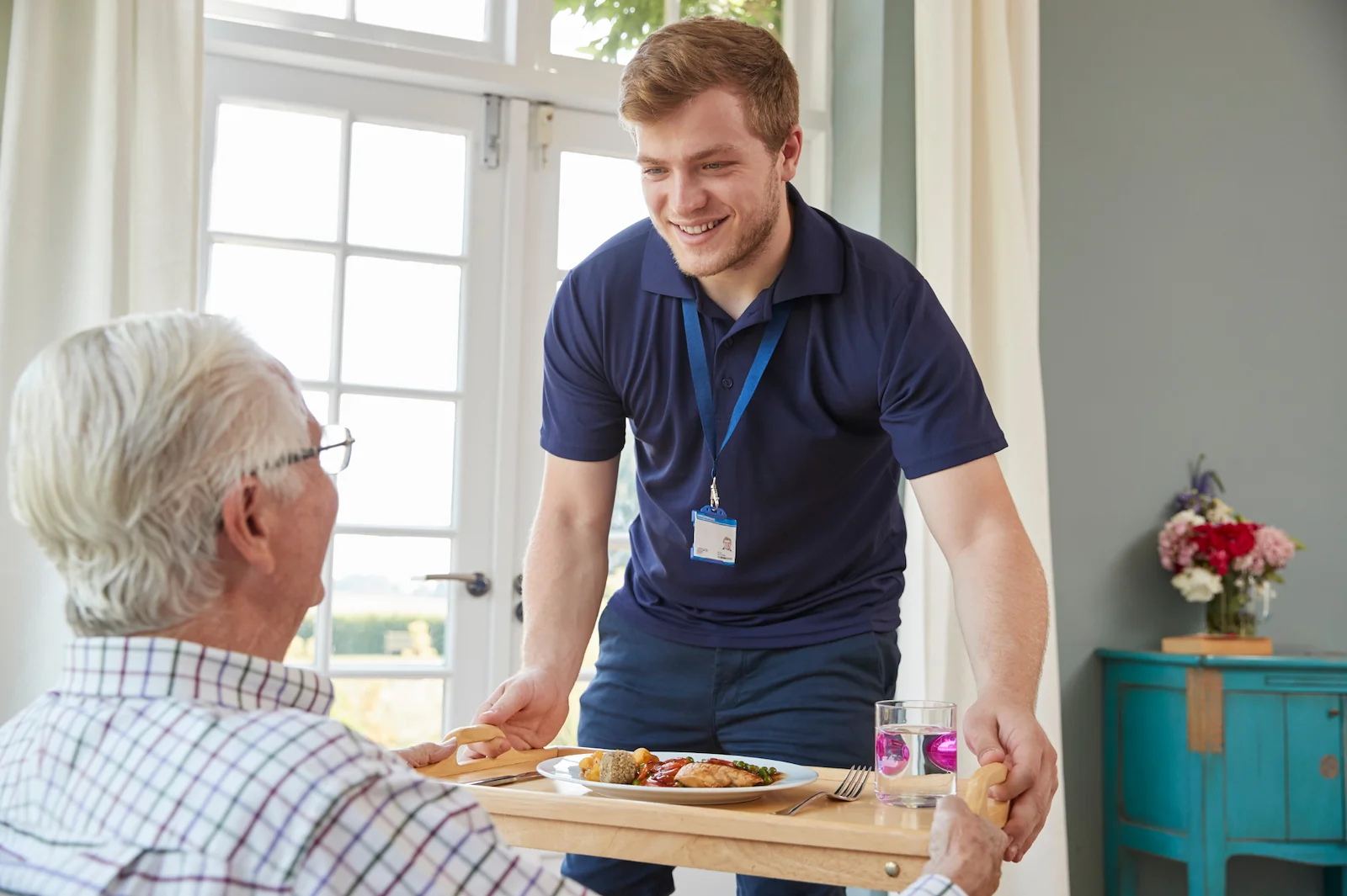 Male caregiver delivering meal to senior man at home