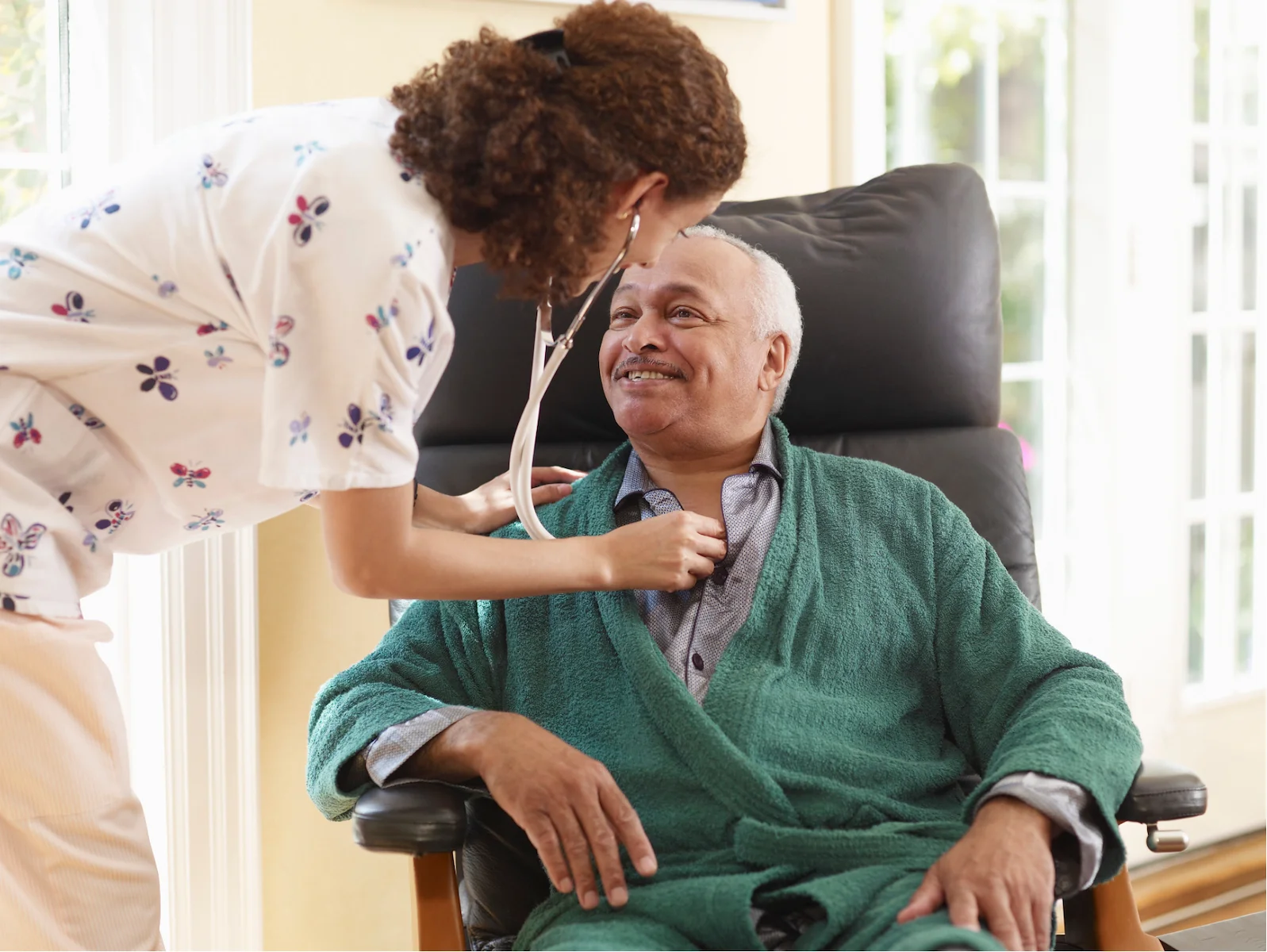 Nurse checking senior man's heartbeat with stethoscope in his home