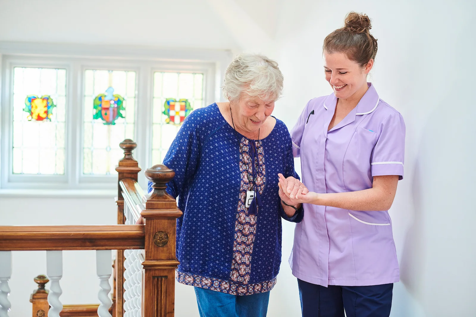 Caregiver helping senior woman walk safely down the stairs at home