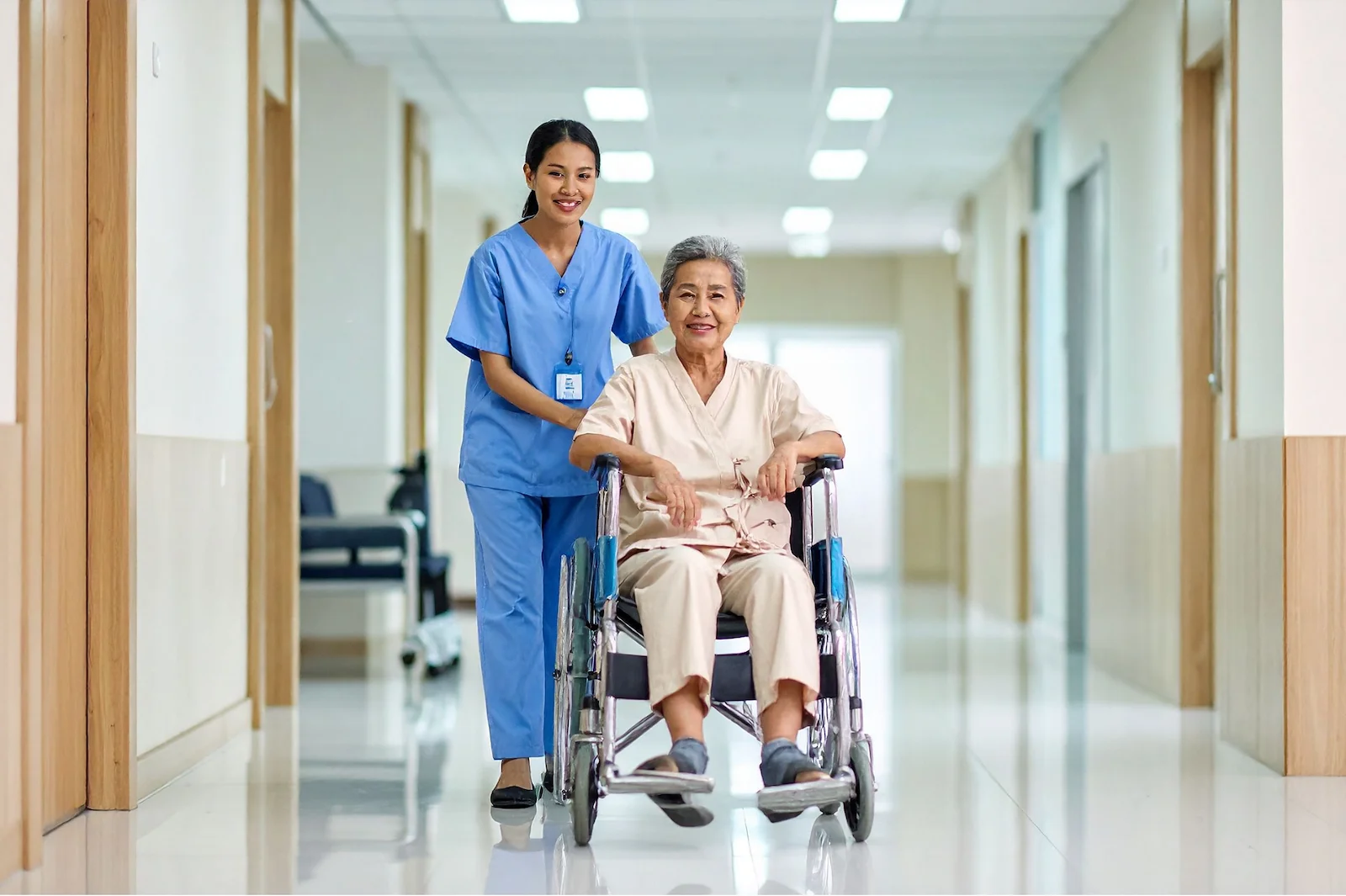 Nurse assisting senior resident in wheelchair through bright facility hallway
