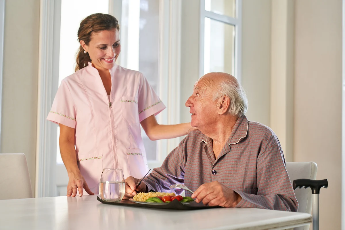 Caregiver serving nutritious meal to senior resident with a smile