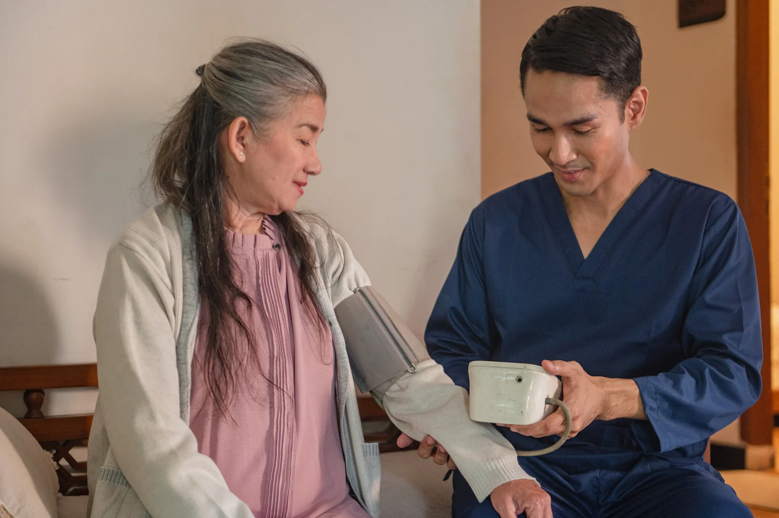 Medical professional checking senior patient's blood pressure at home