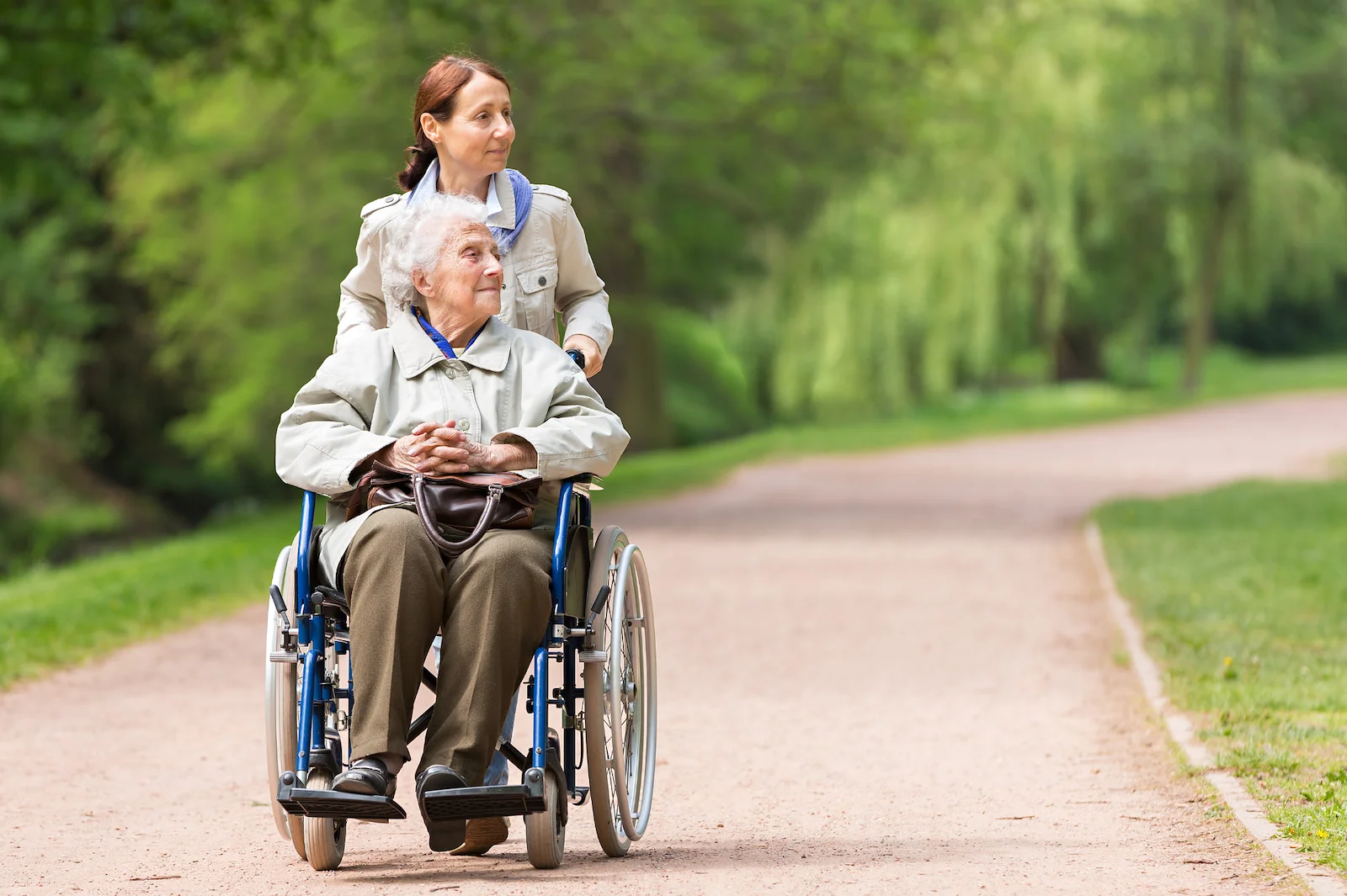 Caregiver accompanying senior on peaceful outdoor walk in wheelchair