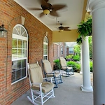 Rocking chairs by the brick wall on the front porch of Charter Senior Living of Hermitage in Hermitage, TN, providing a comfortable and inviting spot for residents to relax in independent living, assisted living, and memory care.