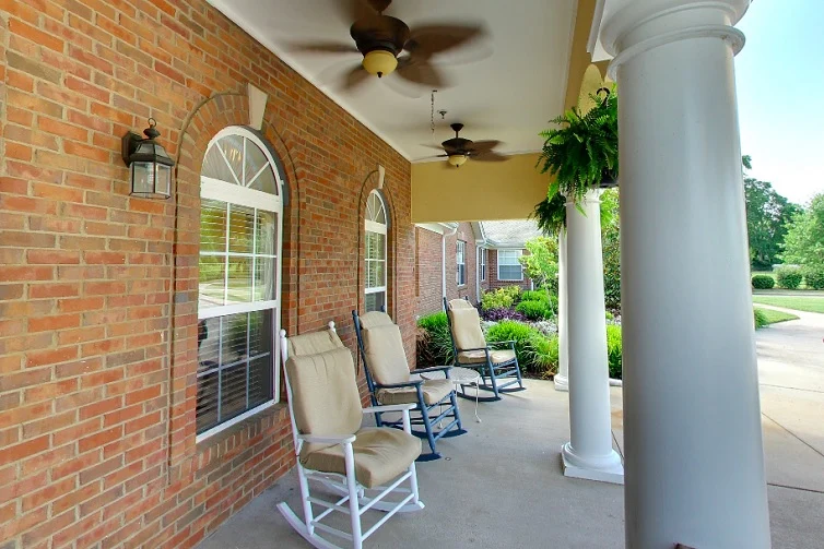 Rocking chairs by the brick wall on the front porch of Charter Senior Living of Hermitage in Hermitage, TN, providing a comfortable and inviting spot for residents to relax in independent living, assisted living, and memory care.