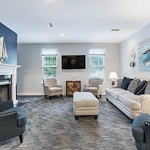 Cozy living room at Charter Senior Living of Hermitage in Hermitage, TN, with comfortable furniture, fireplace, TV, carpet, and windows, welcoming residents in independent living, assisted living, and memory care.