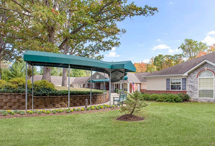 Covered walking path with shade and a bench outside Charter Senior Living of Jackson in Jackson, TN, offering a comfortable outdoor space for assisted living and memory care residents to relax and enjoy fresh air.