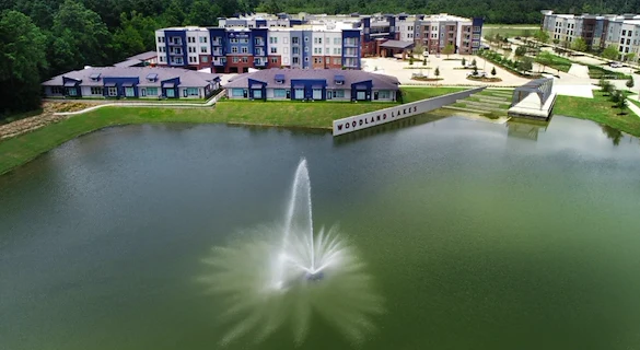 Watermere at Woodland Lakes senior living community offering active adult living and independent living in Conroe, TX, exterior with water fountain in nearby pond