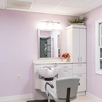 On-site barbershop at Charter Senior Living of Hazel Crest in Hazel Crest, IL, featuring light pink walls, white cabinets, and a large mirror, offering personal grooming services in a cheerful, comfortable setting for assisted living and memory care residents.