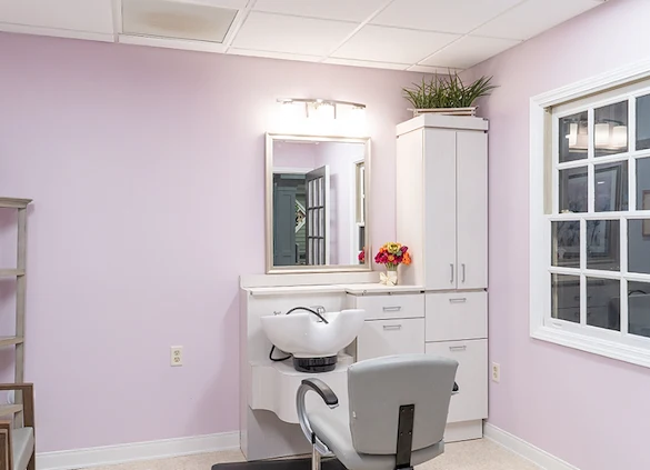 On-site barbershop at Charter Senior Living of Hazel Crest in Hazel Crest, IL, featuring light pink walls, white cabinets, and a large mirror, offering personal grooming services in a cheerful, comfortable setting for assisted living and memory care residents.