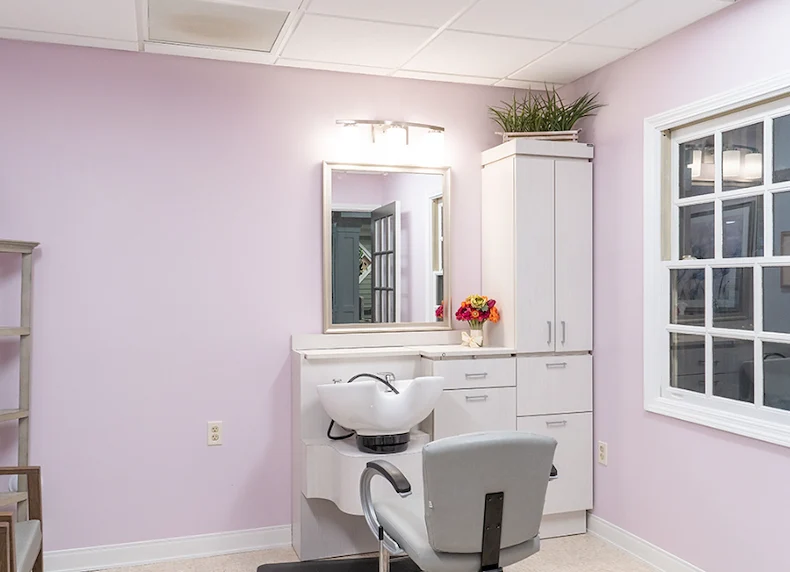 On-site barbershop at Charter Senior Living of Hazel Crest in Hazel Crest, IL, featuring light pink walls, white cabinets, and a large mirror, offering personal grooming services in a cheerful, comfortable setting for assisted living and memory care residents.