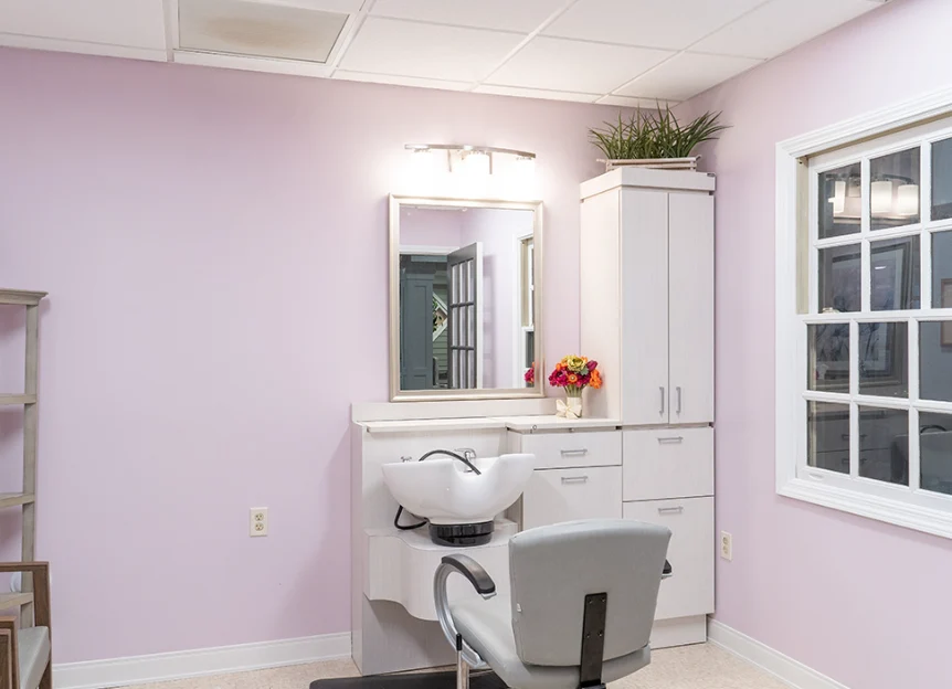 On-site barbershop at Charter Senior Living of Hazel Crest in Hazel Crest, IL, featuring light pink walls, white cabinets, and a large mirror, offering personal grooming services in a cheerful, comfortable setting for assisted living and memory care residents.