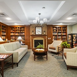 Brightmore of South Charlotte senior living community offering independent living, assisted living, and memory care in Charlotte, NC, library featuring comfortable seating, well-stocked bookshelves, and a cozy fireplace