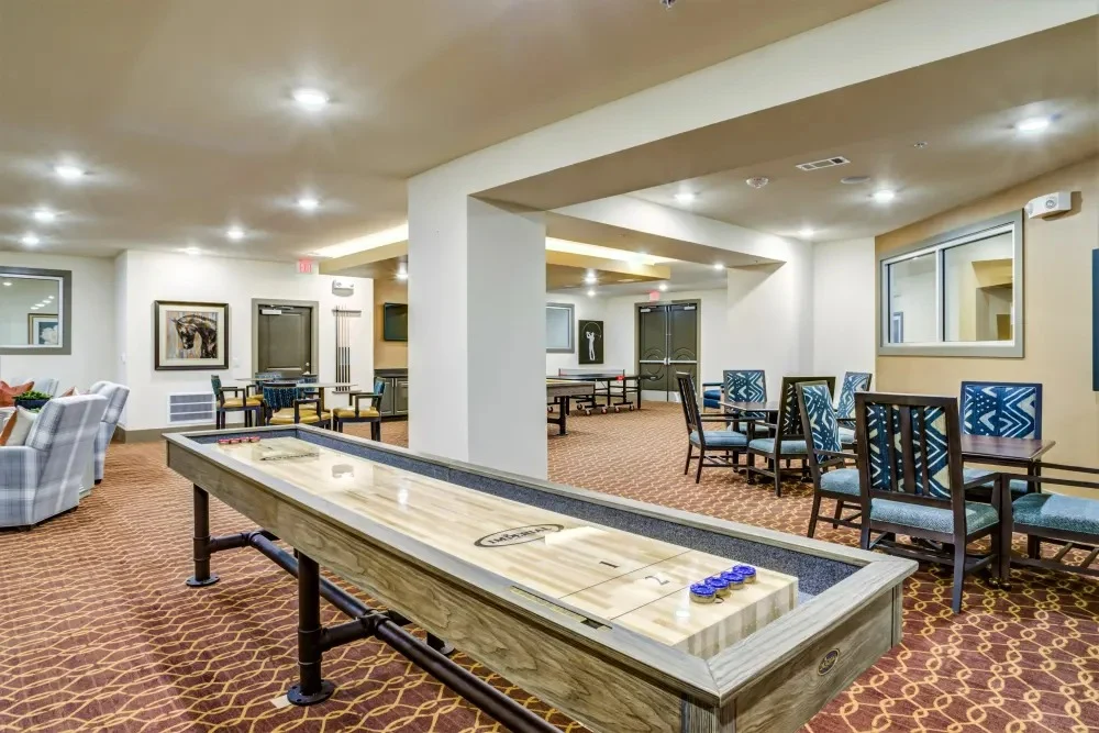Watermere at Round Rock senior living community offering active adult living and independent living in Round Rock, TX, activities room featuring a shuffleboard table and other tables and chairs for games