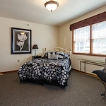 Cozy assisted living bedroom at Charter Senior Living of Hasmer Lake in Jackson, WI, with natural lighting and wall art for a home-like feel.