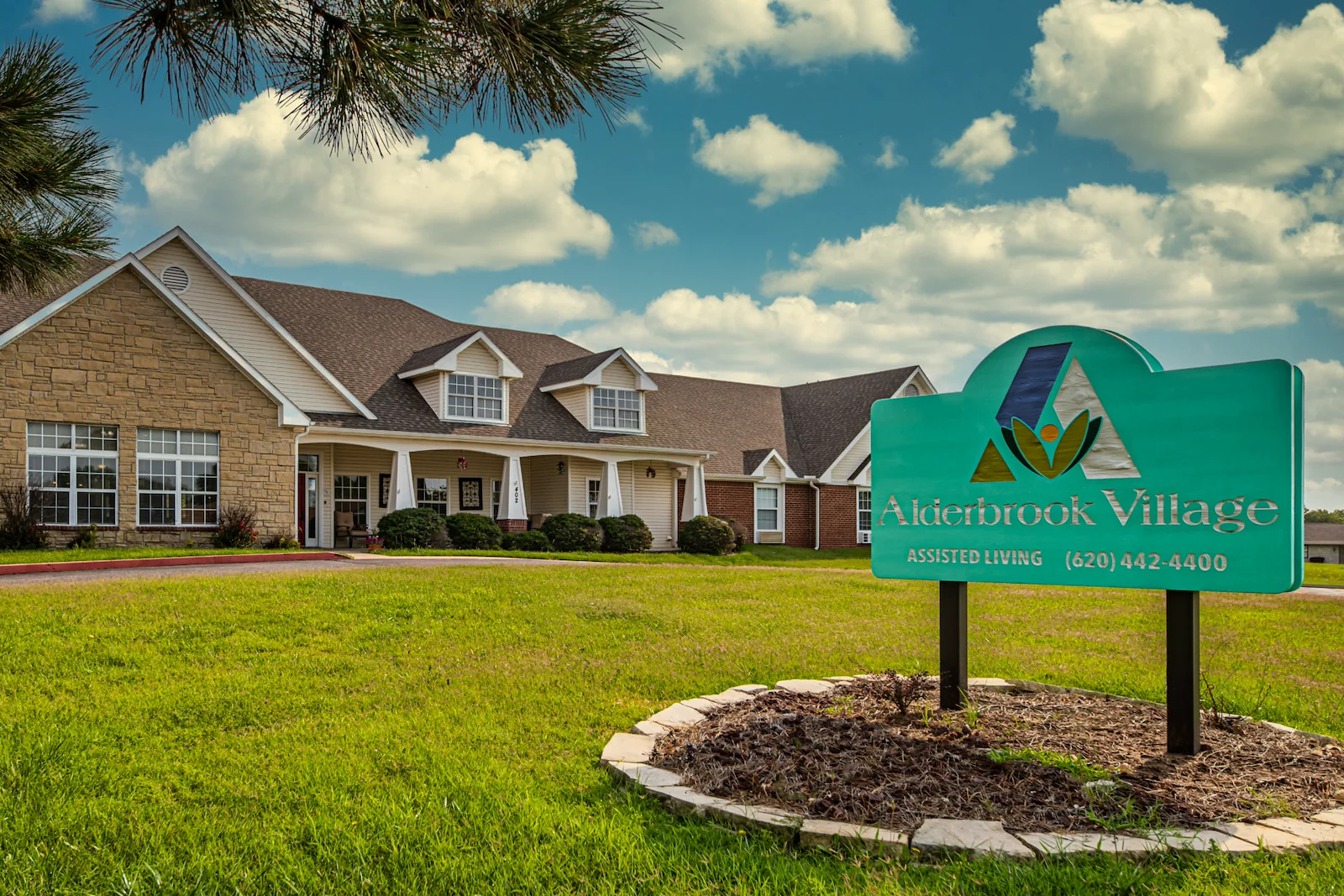 Alderbrook Village assisted living community in Arkansas City, KS, exterior view with community sign in yard and landscaped surroundings