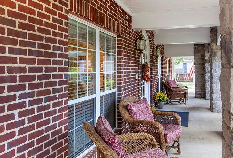 Outdoor furniture set under a covered roof by the brick exterior of Charter Senior Living of Jackson in Jackson, TN, providing a comfortable outdoor gathering space for assisted living and memory care residents.