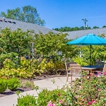 Outdoor patio seating area with table, chairs, and umbrella at Charter Senior Living of Hermitage in Hermitage, TN, surrounded by vibrant flowers and greenery, offering a tranquil outdoor space for seniors in independent living, assisted living, and memory care.