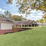 Another exterior view of Charter Senior Living of Jackson in Jackson, TN, featuring the brick building with covered awning and expansive grassy area with mature trees, offering assisted living and memory care in a peaceful setting.