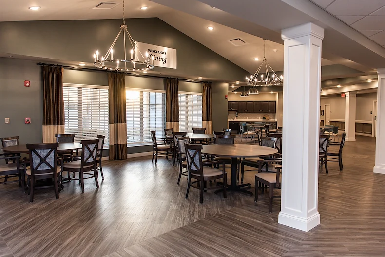 Bright and spacious dining room at Charter Senior Living of Hopkinsville in Hopkinsville, KY, featuring large round tables, elegant lighting, and windows for natural light—designed for comfort in assisted living and memory care.