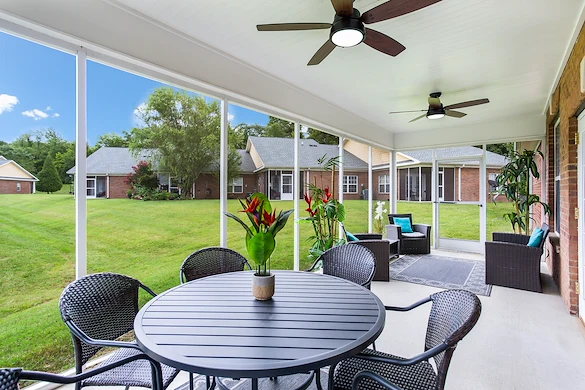 Sunroom with large windows overlooking lush green lawns at Charter Senior Living of Hermitage in Hermitage, TN, featuring comfortable seating and a table, providing a bright, relaxing community space for seniors in independent living, assisted living, and memory care.