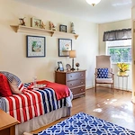 Cozy bedroom with bed, dresser, nightstand, corner chair, and large window providing natural light at Charter Senior Living of Jackson in Jackson, TN, designed for comfort in assisted living and memory care.