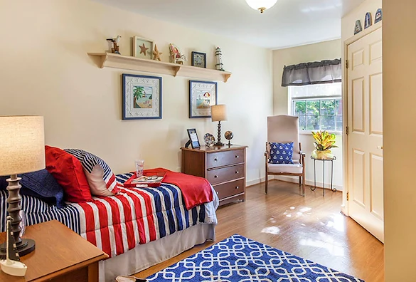 Cozy bedroom with bed, dresser, nightstand, corner chair, and large window providing natural light at Charter Senior Living of Jackson in Jackson, TN, designed for comfort in assisted living and memory care.