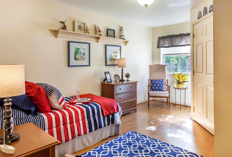 Cozy bedroom with bed, dresser, nightstand, corner chair, and large window providing natural light at Charter Senior Living of Jackson in Jackson, TN, designed for comfort in assisted living and memory care.