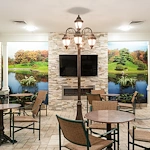 Comfortable common area at Charter Senior Living of Hazel Crest in Hazel Crest, IL, featuring a fireplace with natural landscape wallpaper, TV, chairs, tables, and tile flooring, designed for relaxation and socialization in assisted living and memory care.