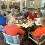 Seniors at Charter Senior Living of Hopkinsville in Hopkinsville, KY, collaborating on a group activity around a wooden table, engaging their minds in assisted living and memory care.