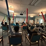 Seniors in assisted living and memory care at Charter Senior Living of Hazel Crest in Hazel Crest, IL, participating in an active group exercise with pool noodles, promoting physical activity and social engagement.
