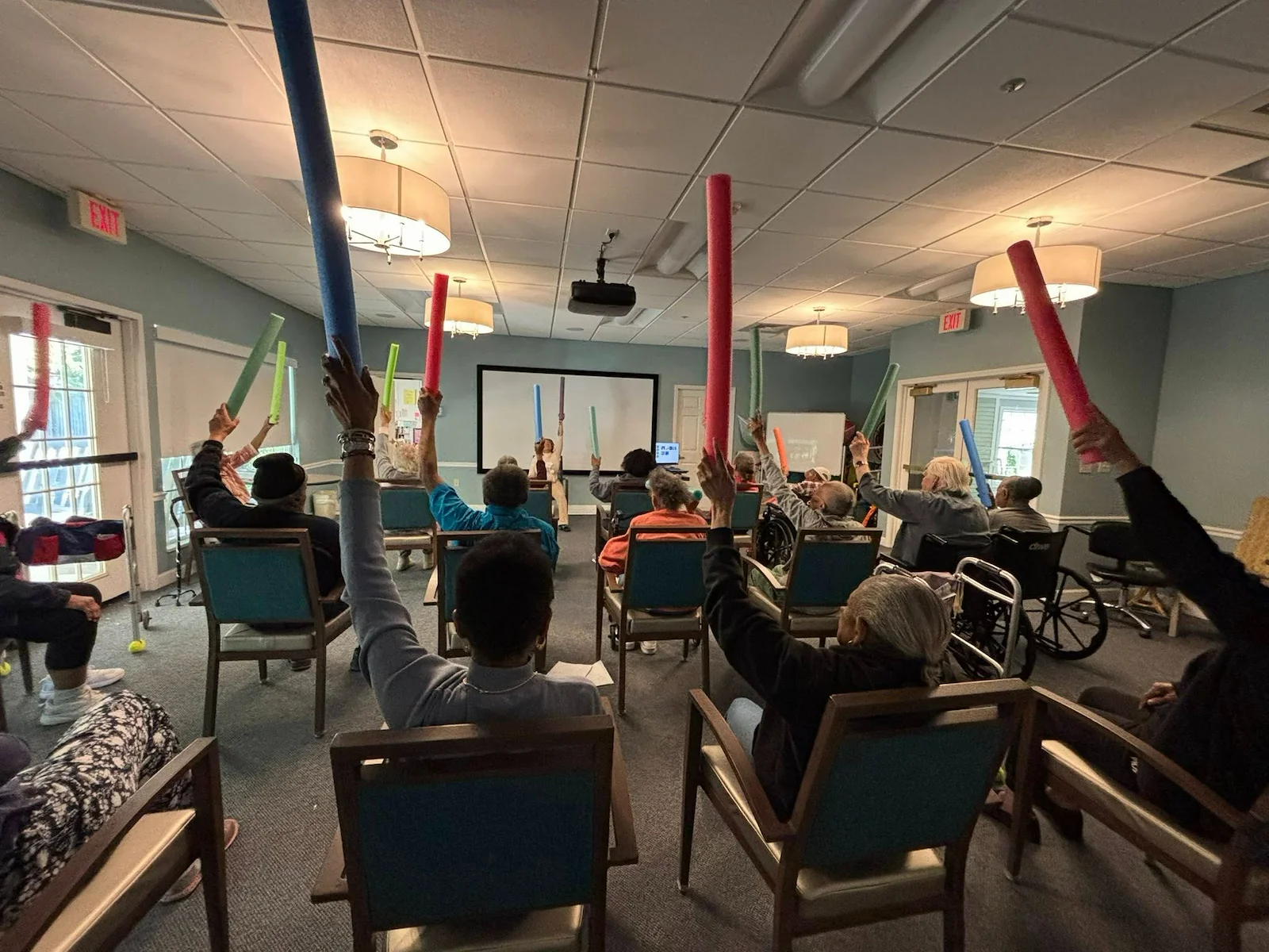 Seniors in assisted living and memory care at Charter Senior Living of Hazel Crest in Hazel Crest, IL, participating in an active group exercise with pool noodles, promoting physical activity and social engagement.